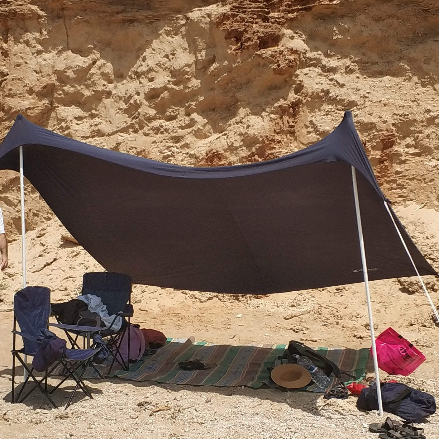 Tent with chairs and a blanket on a sandy beach with rocky cliffs in the background